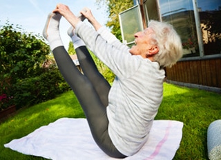 senior woman, 87 years old, very active and flexible, doing exercises in garden at a sunny summer morning